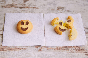 Yellow cookies in the shape of smiling emojis lie on a napkin, while another broken cookie lies...