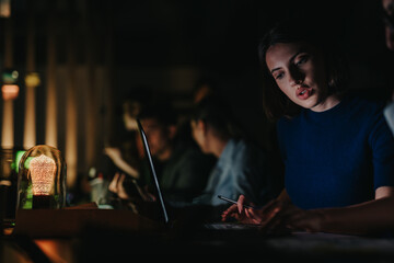 business people engaged in a late-night brainstorming session. The dimly lit environment creates a focused atmosphere, highlighting teamwork and collaboration among colleagues working on a project.