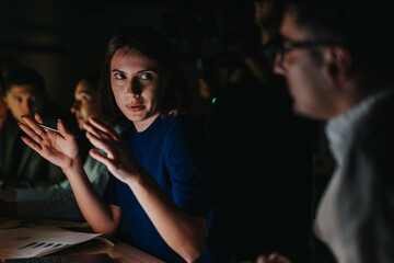 A group of business people engaged in an intense brainstorming session at night, focusing on...