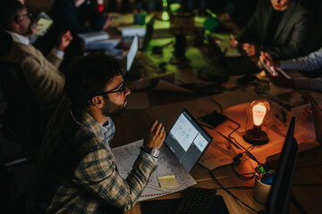 A group of people working late, discussing ideas, and analyzing data for an important project. The atmosphere is focused and collaborative, highlighting teamwork and dedication in a modern setting.