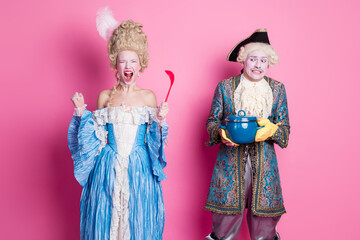 A whimsical couple in costumes enjoys hilariously themed party. The woman joyfully holds a spatula, while the man humorously presents a pot