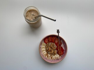 Summer breakfast yogurt bowl with strawberries banana peanut butter cashews and granola with iced coffee latte on white background isolated flat lay 