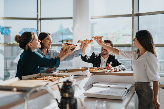 A group of colleagues enjoy a casual pizza party in a modern office setting, celebrating teamwork and success. Their cheerful interaction highlights a positive and collaborative work environment. - Powered by Adobe