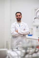 vertical Portrait of smiling dentist posing with crossed arms in his clinic