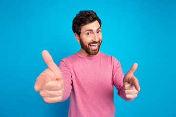 Cheerful bearded man showing double thumbs-up in pink sweater on blue background for positive and promotional concepts