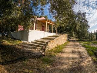 Small building with porch and steps nestled among trees beside a dirt path.