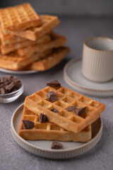 photo Delicious golden brown waffles stacked with chunks of rich chocolate, served with a warm beverage, creating a perfect breakfast or brunch experience in a cozy setting