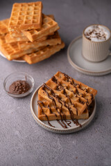 photo Delicious homemade waffles drizzled with chocolate, served on a plate alongside a frothy coffee and a dish of chocolate spread, perfect for a sweet breakfast treat