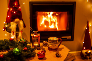 A mug of hot chocolate with marshmallows in wooden table in front of a fireplace as a background.
