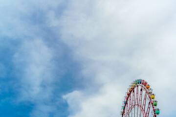 Fototapeta premium Colorful ferris wheel against blue sky with clouds and copy space.