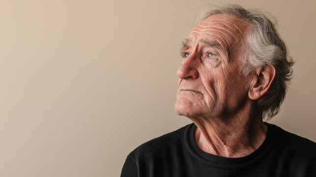 Portrait of a contemplative old man with wrinkles looking upwards against a neutral background, conveying emotions of hope, concern or deep thought