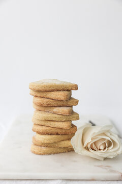 Close-up of a white rose on a table next to a Stack of homemade heart shaped shortbread biscuits