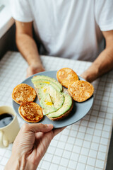 man has breakfast at home in kitchen. plate with avocado toast, pancakes and black coffee. bright and cozy place. healthy eating, vegetarian. top view of food. nutritious lunch, delicious balanced.