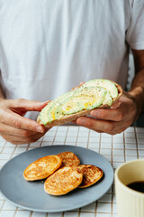 man has breakfast at home in kitchen. plate with avocado toast, pancakes and black coffee. bright and cozy place. healthy eating, vegetarian. top view of food. nutritious lunch, delicious balanced.