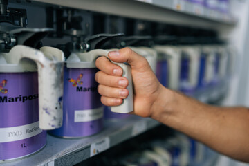 Close-up hands of unrecognizable auto painter male choosing appropriate color for car dyeing, make choice from cans. Mechanic selection colors for car painting. Concept of car service, maintenance.
