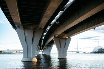 view from below of arches of suspension road. bridge over water, expressway against sky. Transport...