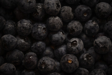 a bright yellow classic Mini Cooper driving on a paved street, likely in a European town. The car, a right-hand drive model, is the primary subject and is positioned slightly off-center to the left.