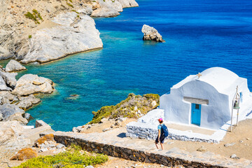 Woman tourist with backpack walking on path to Agia Anna beach and passing by white small Greek...