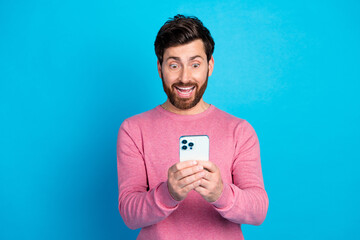 Excited man in casual wear holding smartphone against blue background, expressing joy and surprise, representing modern technology and communication