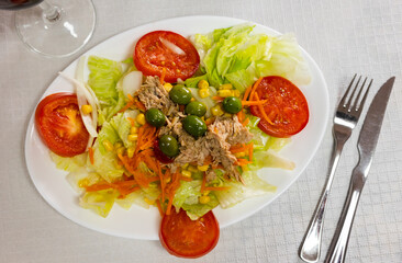 Colorful light salad of chopped fresh lettuce with ripe tomatoes, sliced grated carrot, olives and crushed canned tunny served for dinner