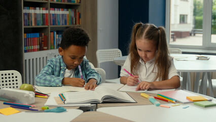 Multiethnic little kids classmates African boy Caucasian girl daughter son elementary school education pupils students children study learn write at desk together schoolgirl schoolboy lesson homework