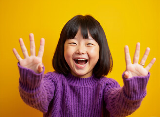 Asian girl raising hands on vibrant yellow background