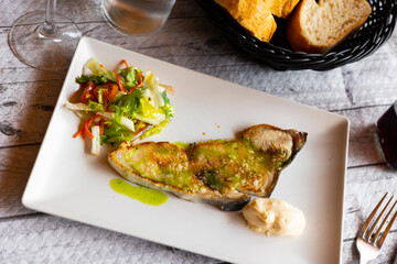 Delicious seared mako shark steak seasoned with aromatic herb oil on white plate with vibrant side salad of fresh lettuce, tomato and carrot and dollop of creamy sauce, set on wooden table