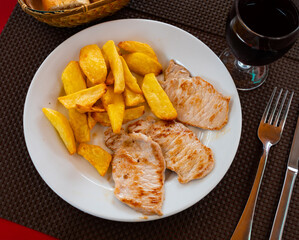 Roasted pork and potato cut into pieces dished up in a plate on the laid restaurant table