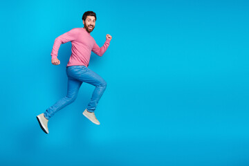 Energetic young man in casual fashion jumping against a vivid blue background, showcasing fun and excitement