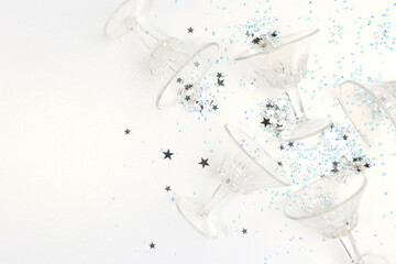 Small crystal glasses and stars confetti scattered on a silver colored glittering background. Place for your design.