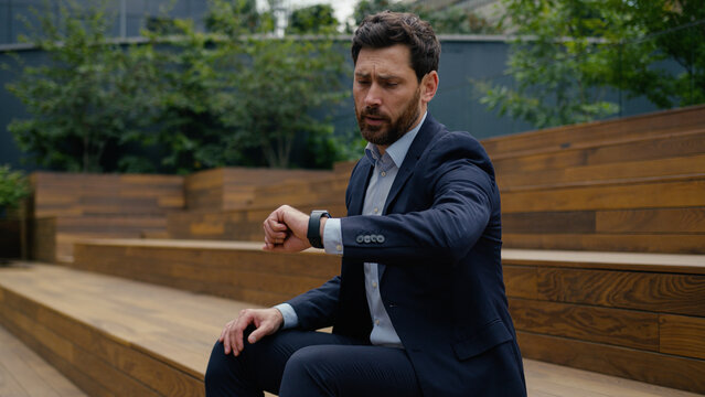 Businessman Caucasian man male entrepreneur business client sit outside upset sad worried guy employer tired waiting late meeting in city check time looking at wristwatch lateness delay date outdoors