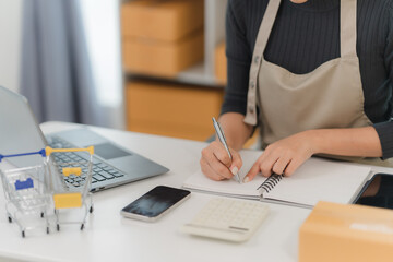 Small Business Owner Managing Orders: A close-up shot of a female entrepreneur meticulously writing...