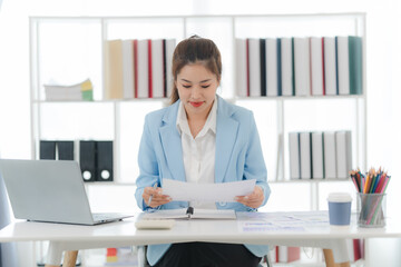 Focused and Confident: A young businesswoman in a sleek blue blazer meticulously reviews documents...