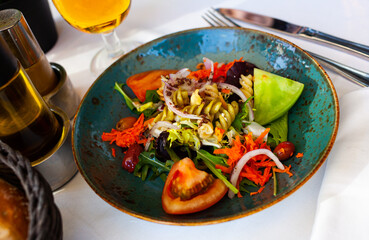 Portion of healthy salad with pasta, avocado, tomatoes, greens, carrot and onion