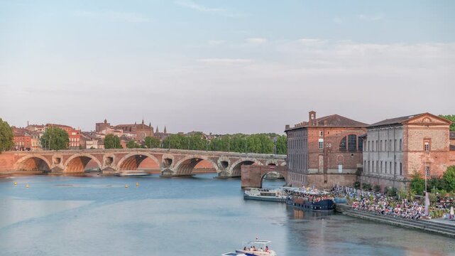Garonne River and Pont Neuf timelapse with Museum of the History of Medicine in downtown Toulouse, France. This Renaissance arch bridge reflects in water under a blue sky. Waterfront with green trees