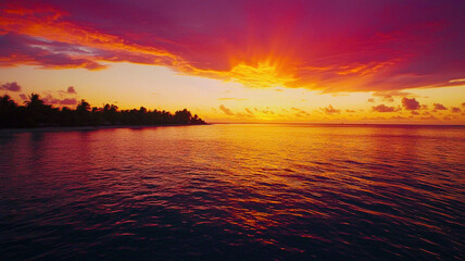 Obraz premium A vibrant tropical sunset over calm ocean waters, featuring vivid shades of orange, pink, and purple blending into a dramatic sky, with palm trees silhouetted on the horizon.