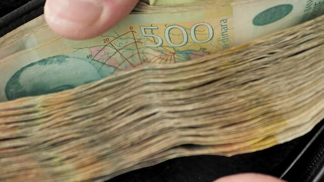 The hand of a man demonstratively opening his wallet shows many piles of banknotes and turns over with his fingers the Serbian dinar notes of 500 dinars. Serbian currency