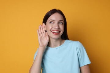 Woman showing hand to ear gesture on orange background