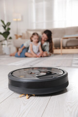 Mother spending time with her daughter in room, focus on robotic vacuum cleaner