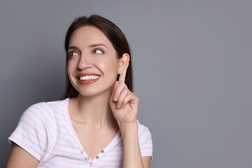 Woman showing hand to ear gesture on grey background, space for text
