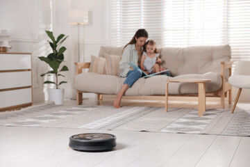 Mother spending time with her daughter in room, focus on robotic vacuum cleaner