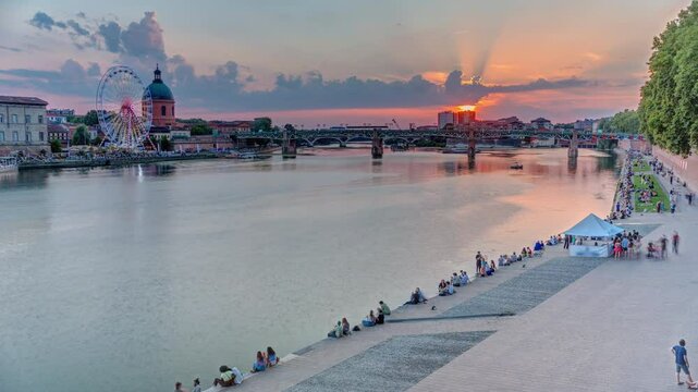 Aerial view of La Grave Hospital with Saint-Pierre Bridge. Port de la Daurade park along the Garonne River timelapse in Toulouse, France. Sunset colorful clouds, ferry at dock and riverside atmosphere