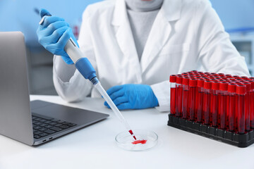 Laboratory testing. Doctor dripping blood sample into Petri dish at table indoors, closeup