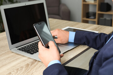 Businessman using smartphone and laptop at wooden table, closeup. Modern technology