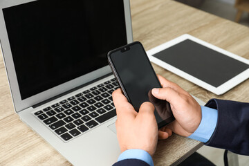 Businessman using smartphone near laptop at wooden table, closeup. Modern technology