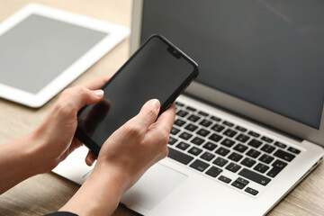 Businessman with smartphone near laptop at table, closeup. Modern technology