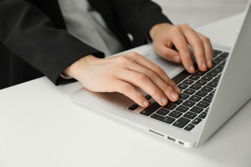 Businesswoman using laptop at white table indoors, closeup. Modern technology