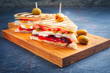 Traditional club toast sandwich with ham, cheese and egg served with vegetables as close-up on a wooden cutting board
