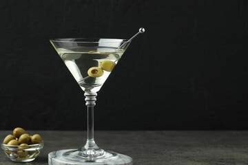 Martini cocktail with olives in glass on grey table against black background, space for text