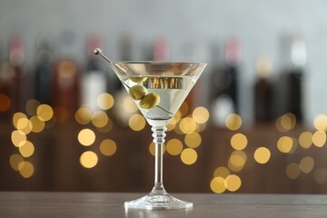 Martini cocktail with olives in glass on wooden table against blurred background. Bokeh effect